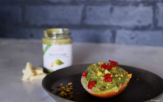 Ein Teller mit einer Brioche-Hälfte, die mit Matcha Schokoladencreme von Grashoff bestrichen und mit Himbeeren und Pistazien bestreut worden ist.