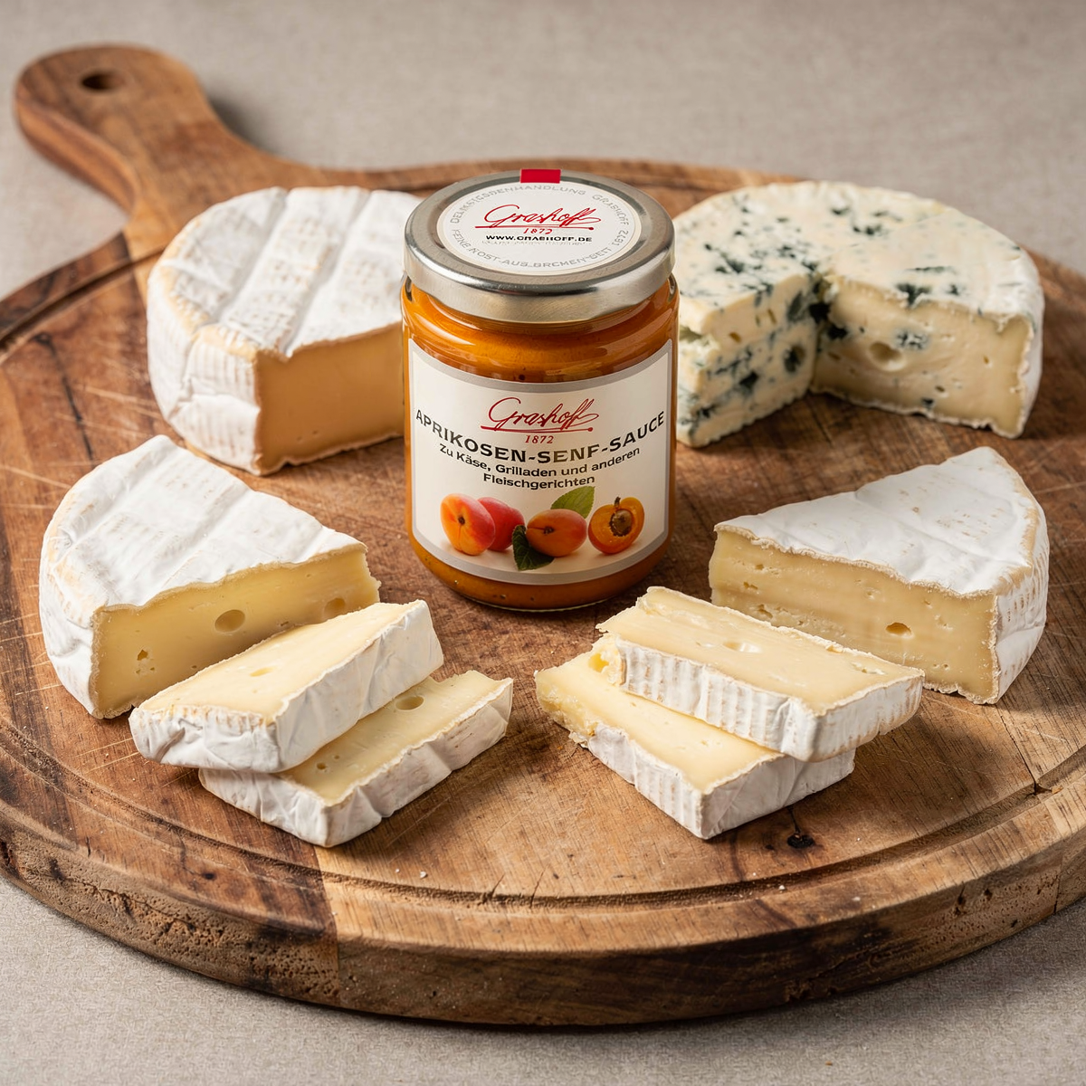 Glas Grashoff Aprikosen-Senf-Sauce mit verschiedenen Weichkäsen und Blauschimmelkäse auf einem rustikalen Holzbrett.