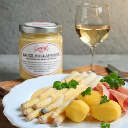 Ein Teller mit Spargel, Kartoffeln und Schinken. Im Hintergrund ein Glas Sauce Hollandaise von Grashoff und ein Glas Weißwein.